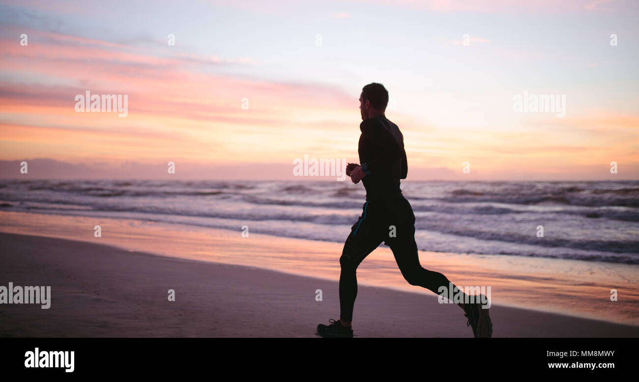 Uomo che corre sulla spiaggia di mattina. Maschio sano jogging sulla riva del mare. Foto Stock