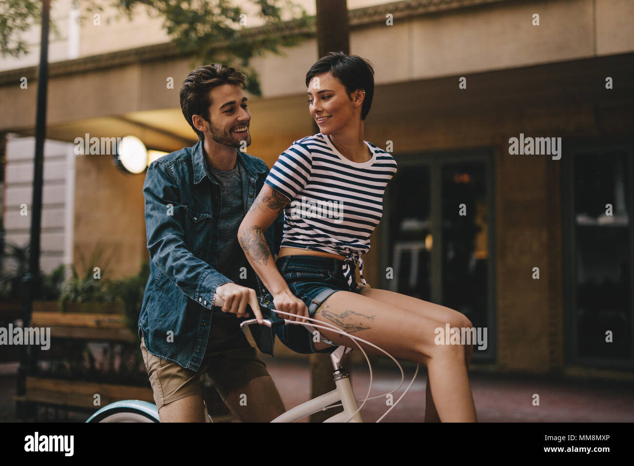 Felice giovane uomo cavalca una bicicletta con donna seduta sul manubrio. Coppia romantica godendo di corsa in bicicletta in città. Foto Stock