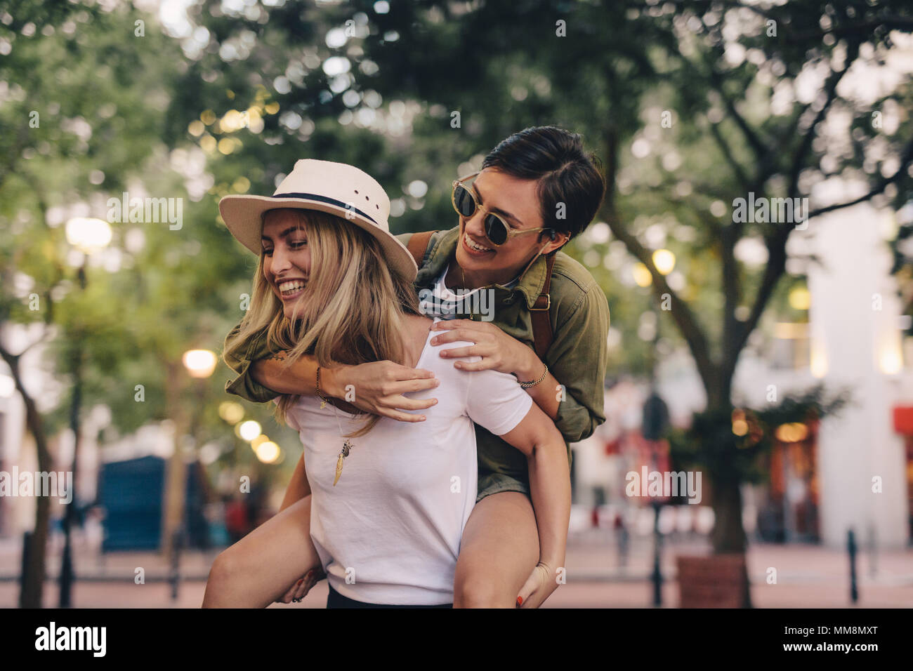La donna che porta il suo amico femmina sulla sua schiena e camminare sulla strada. Amici di sesso femminile godendo insieme all'esterno. Foto Stock
