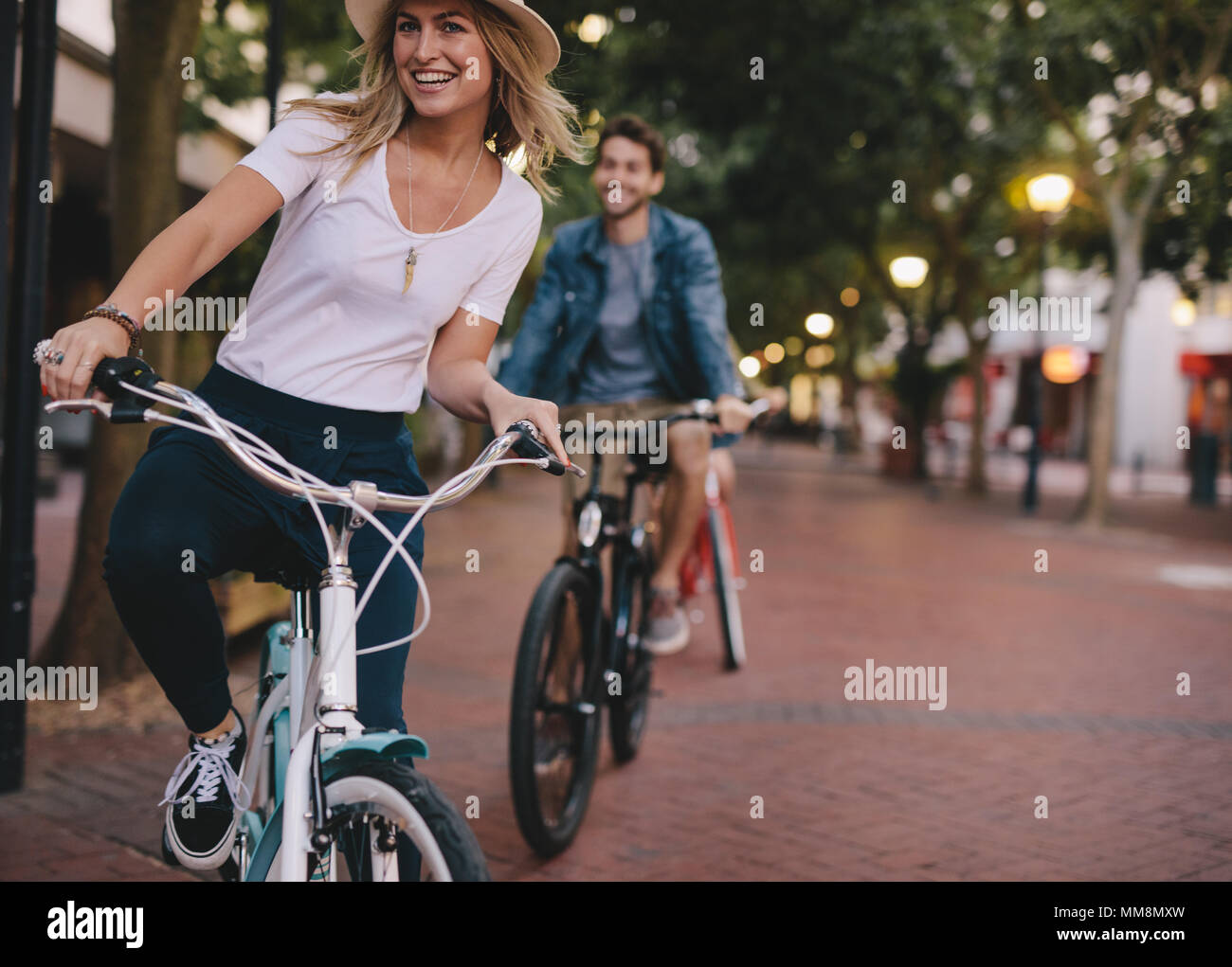 Donna ciclismo su strada di città con gli amici. Gli amici sorseggiando una corsa in bicicletta all'esterno. Foto Stock