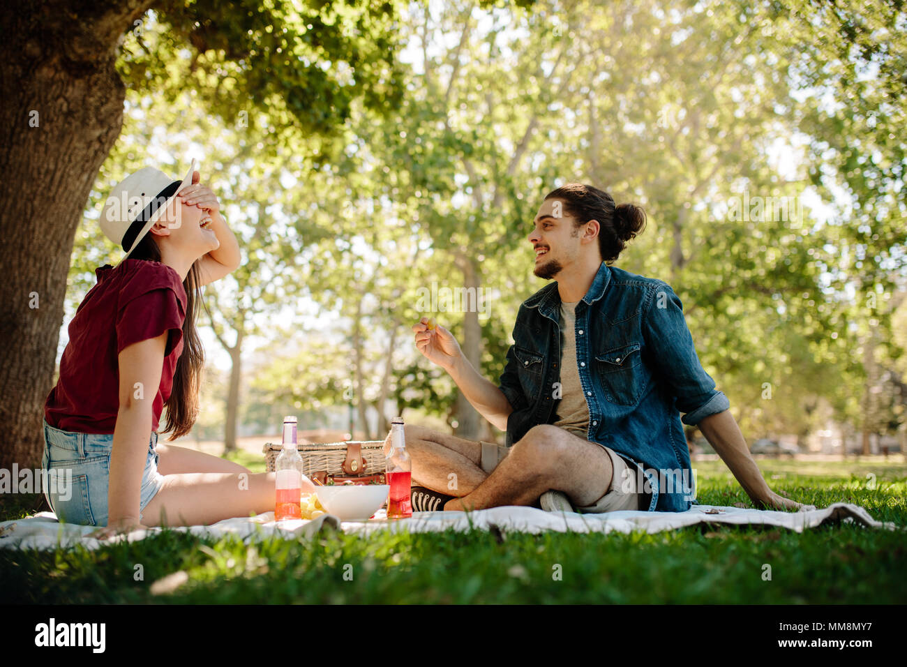 Accoppiare la riproduzione di un gioco su picnic al parco. Donna che copre la sua gli occhi con uomo tenendo un frutto in mano. Foto Stock
