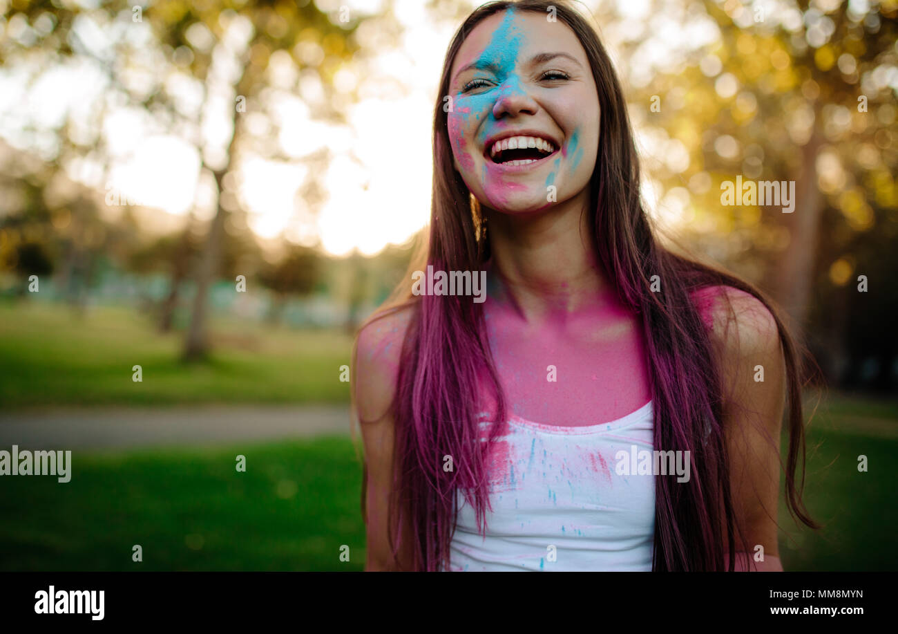 Bella donna con polvere colorata cosparsa sul suo viso. Ragazza sorridente giocando con i colori durante Holi festival al parco. Foto Stock