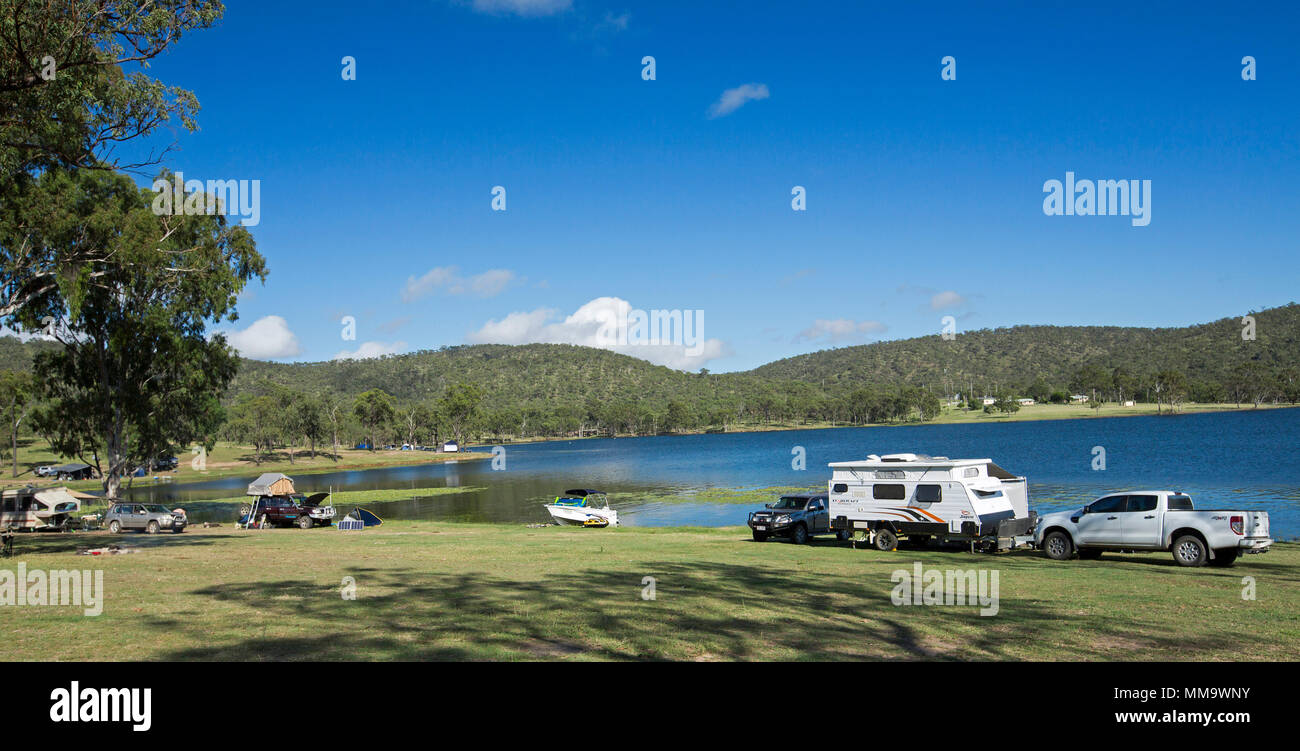 Vista panoramica di camper con tende e caravan a fianco di acque blu del lago in uno splendido paesaggio boscoso sotto il cielo blu a diga Eungalla Australia Foto Stock