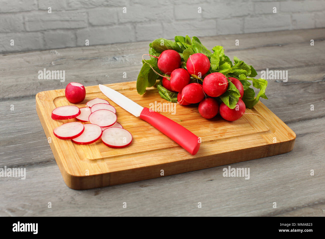 Mazzetto di fresco radicchio rosso su un tagliere di legno, ceramica coltello, con alcuni del rafano tagliato in piccoli cerchi. Foto Stock