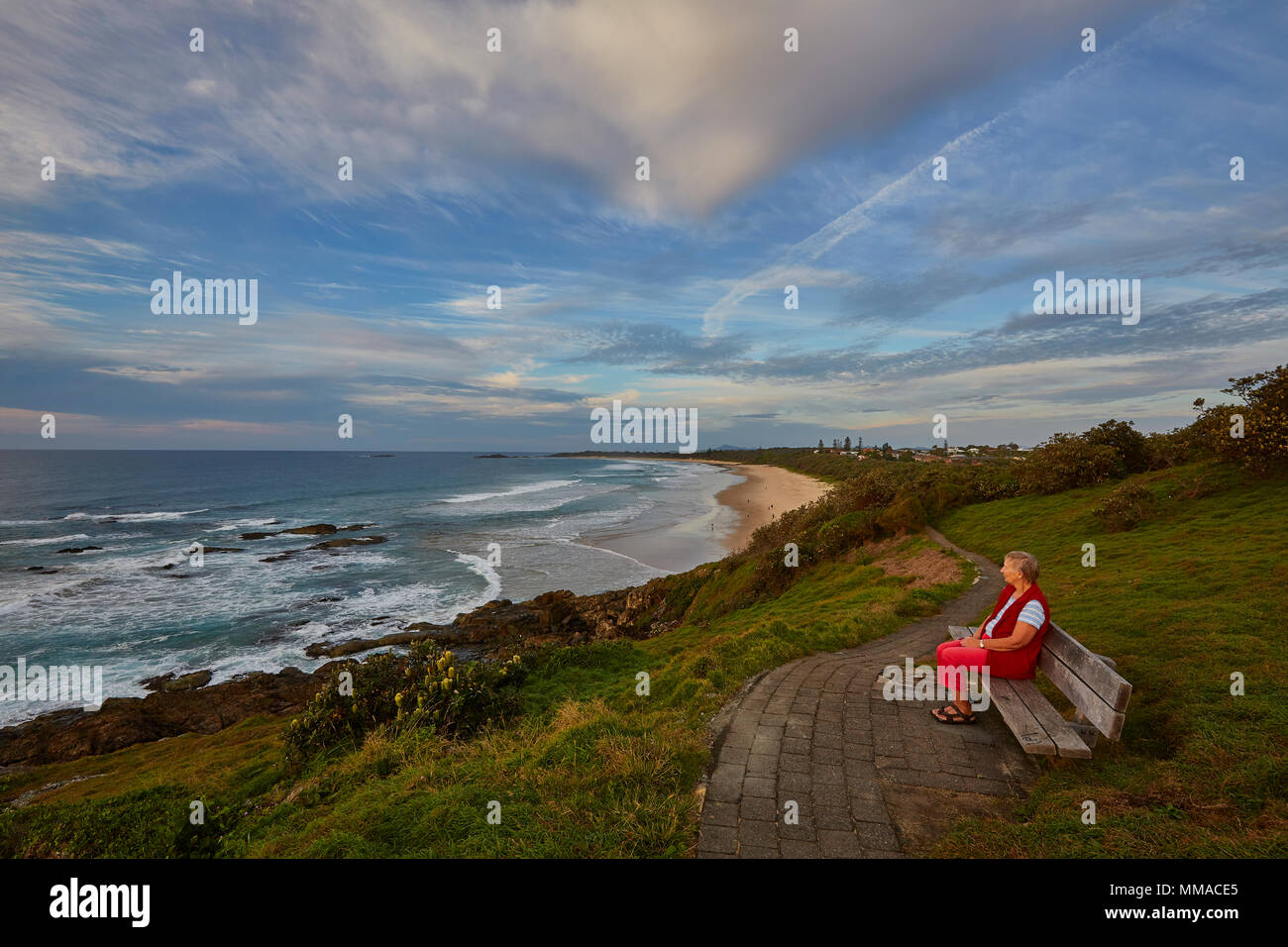 Una donna sul suo proprio seduto su una panchina alla capezzagna Boambee guardando Murray's Beach, Nuovo Galles del Sud, NSW, Australia Foto Stock