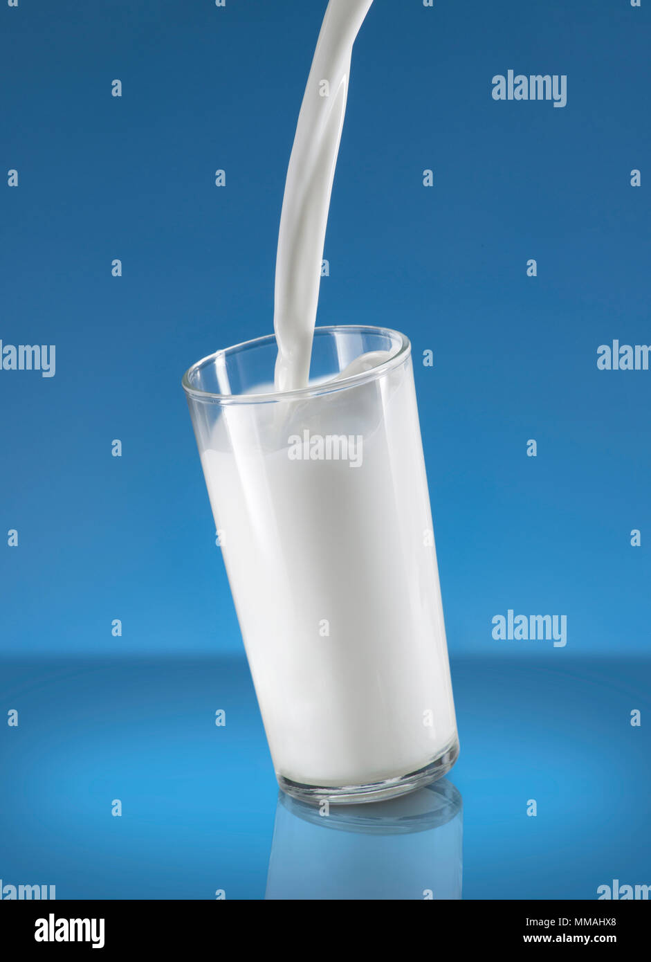 Versare il latte Splash in un bicchiere su sfondo blu Foto Stock