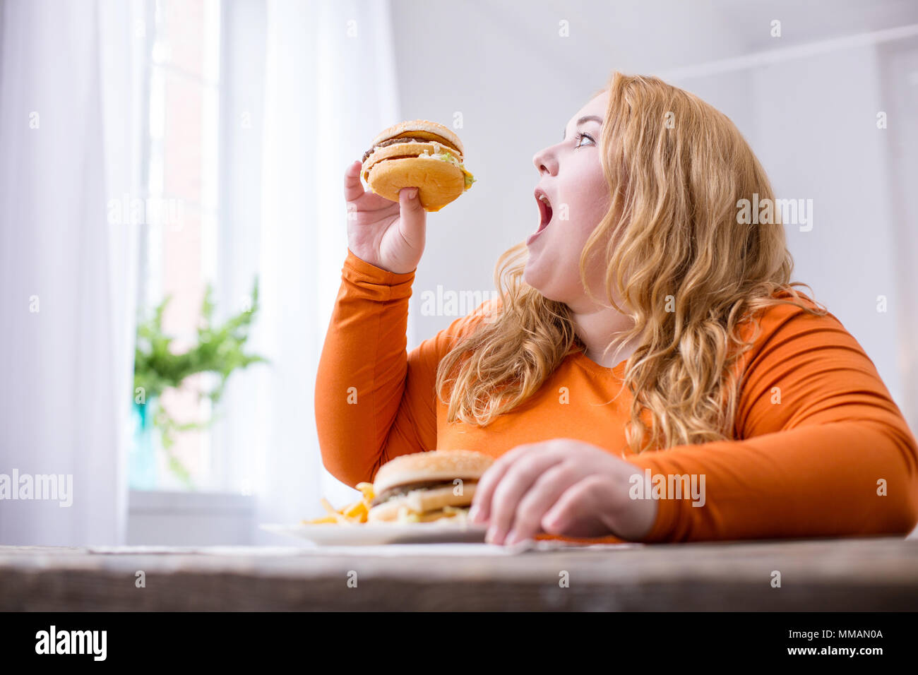 Contenuto grasso donna mangiare patatine fritte e panini Foto Stock