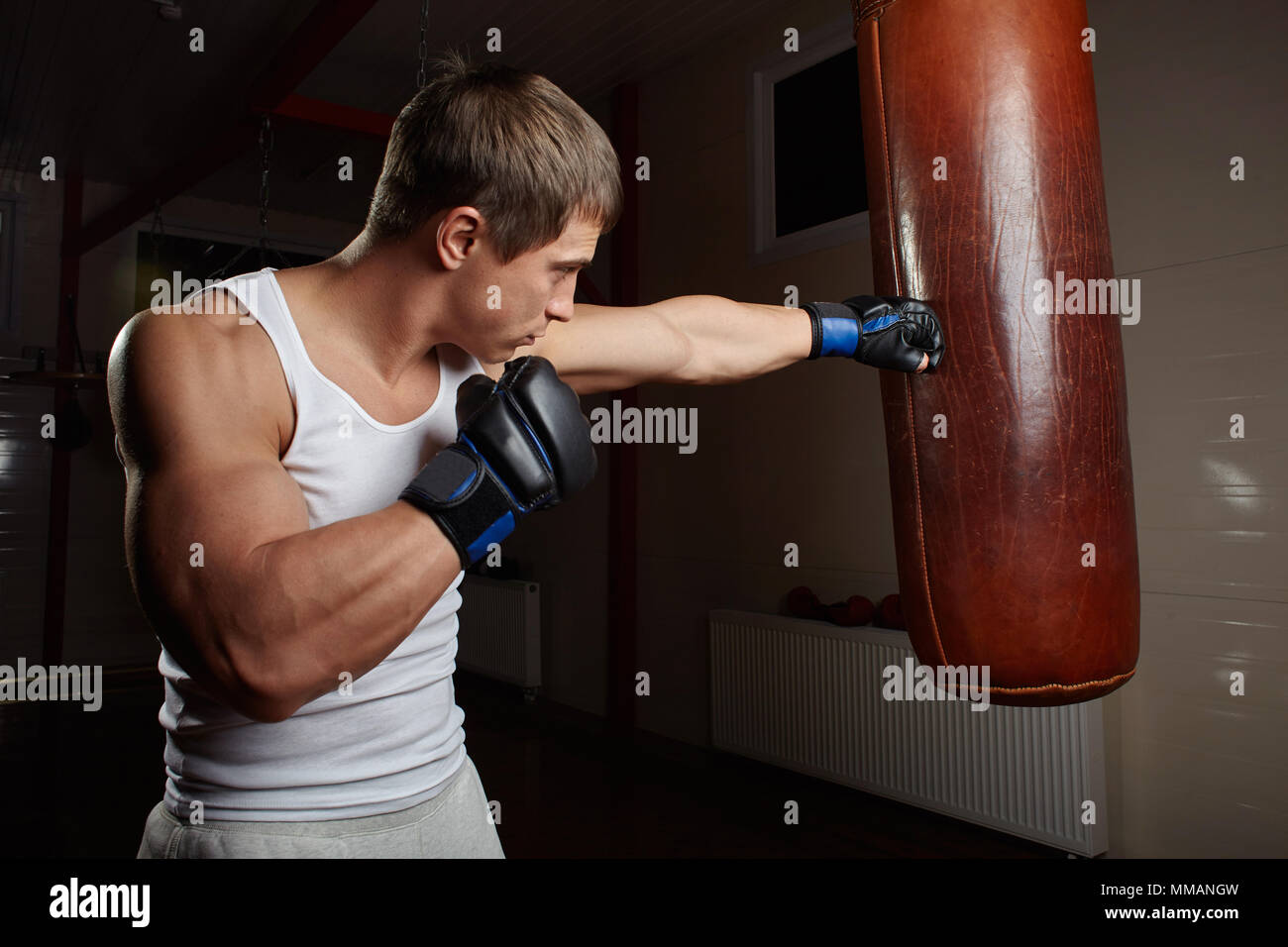 Giovane maschio muscolare boxer punch sacco da boxe in palestra interno Foto Stock