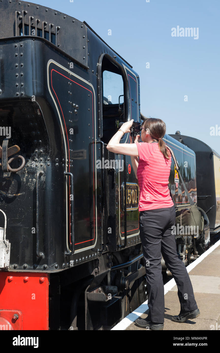 Emozionato femmina appassionato di treno di scattare fotografie di lucido, conserve di locomotiva a vapore, fermo sulla piattaforma, su un gloriosamente mattina di sole in maggio. Foto Stock