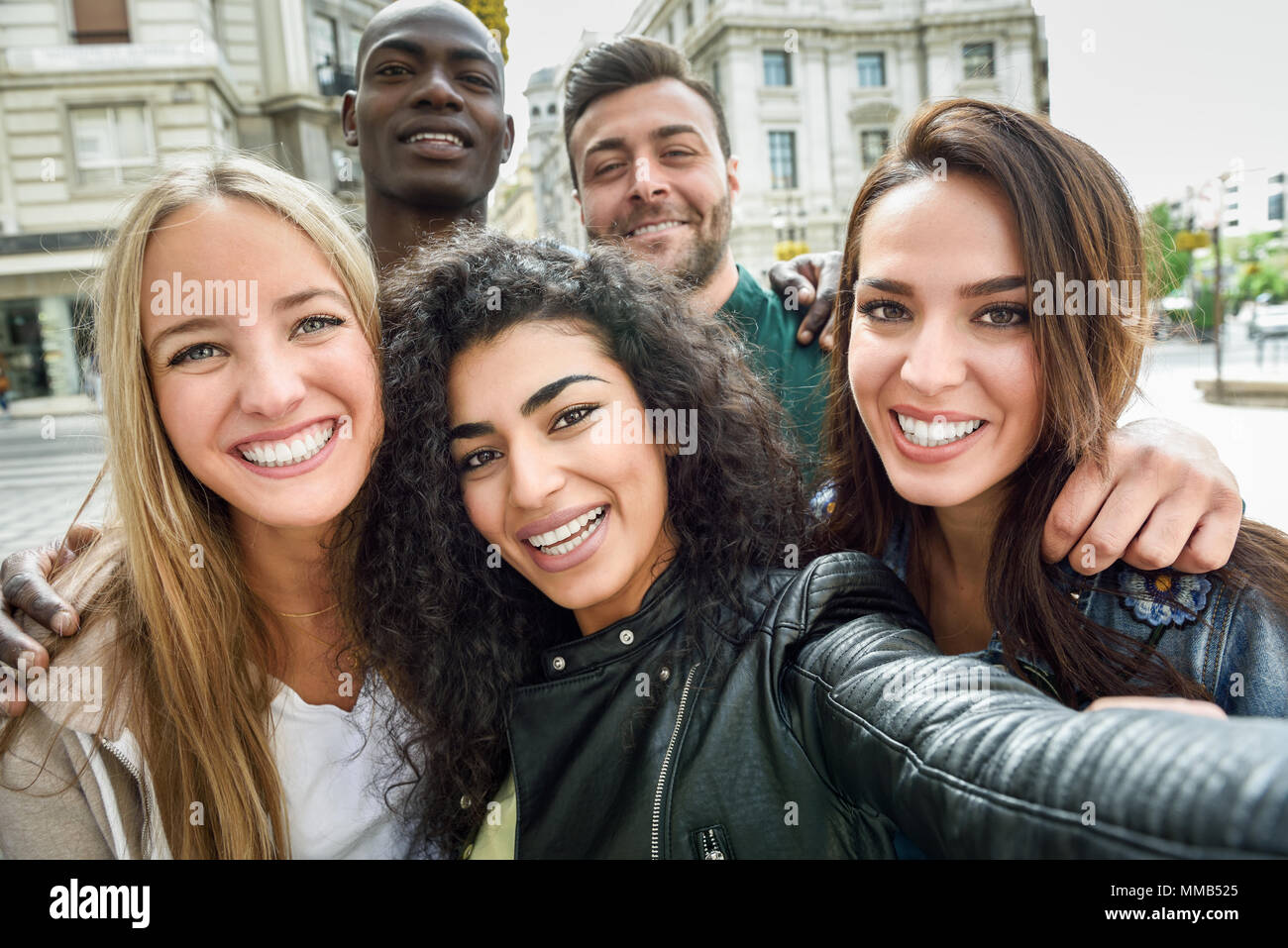 Gruppo multirazziale di amici prendendo selfie in una strada urbana con una donna musulmana in primo piano. Tre giovani donne e due uomini che indossano un abbigliamento informale. Foto Stock