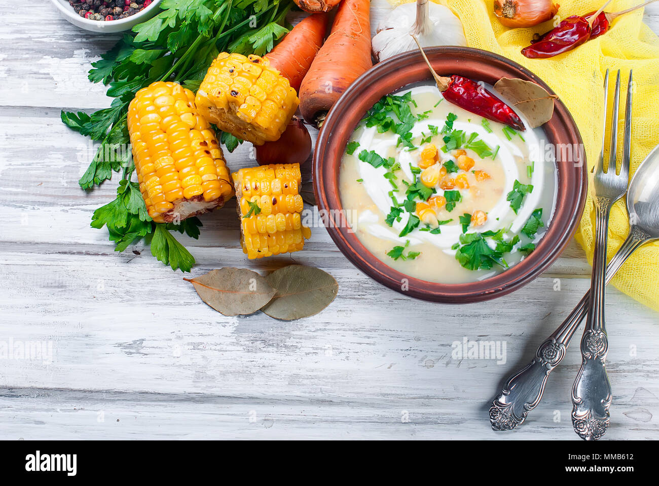 Zuppa dal mais con panna acida in una piastra di ceramica e gli ingredienti per la zuppa, pannocchie di granoturco, verdi, le carote. Mangiare sano Foto Stock