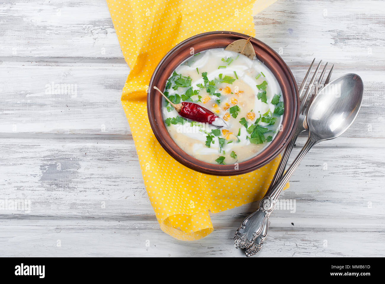 Zuppa dal mais con panna acida in una piastra di ceramica e gli ingredienti per la zuppa, pannocchie di granoturco, verdi, le carote. Mangiare sano Foto Stock