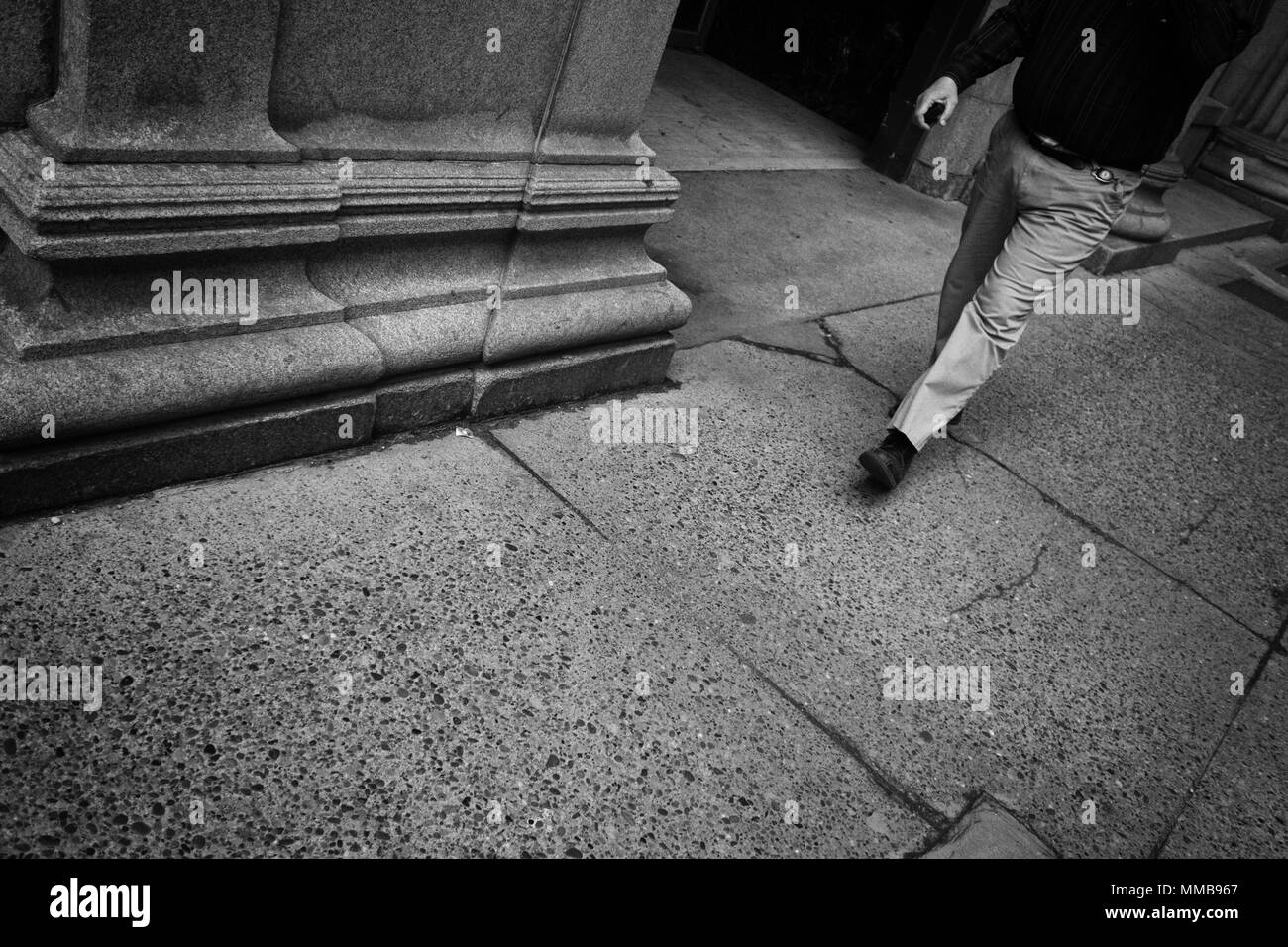 Una immagine in bianco e nero di un uomo di piedi come egli cammina lungo un marciapiede in città Foto Stock