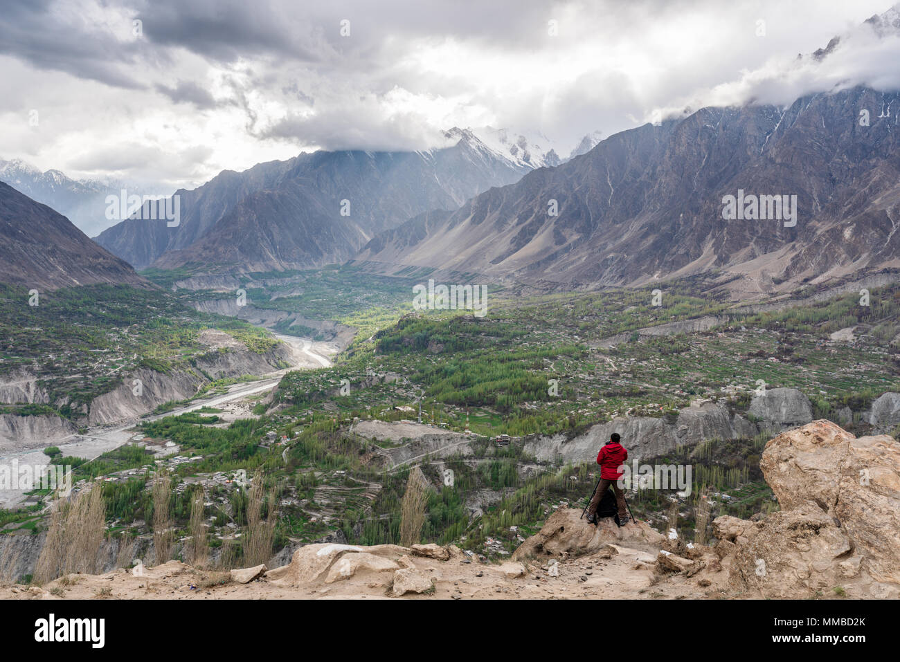 Fotografo in giacca rossa tenendo il paesaggio fotografia sul picco di montagna scogliera di Hunza valley in Pakistan Foto Stock