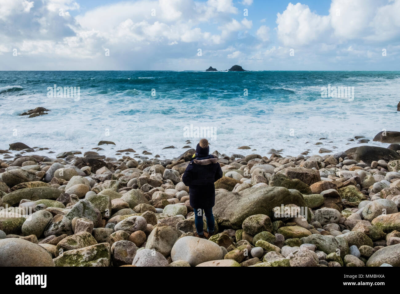 Una donna in piedi sulle rocce che si affaccia sul litorale della Cornovaglia, e le onde che si infrangono. Foto Stock