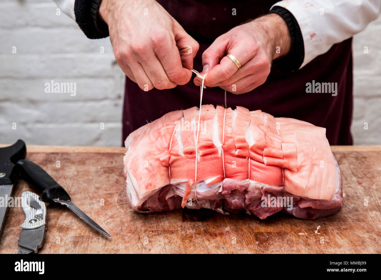 Chiusura del macellaio grembiule da indossare in piedi presso un macellaio in legno del blocco, preparare un laminato pancetta di maiale utilizzando la stringa. Foto Stock