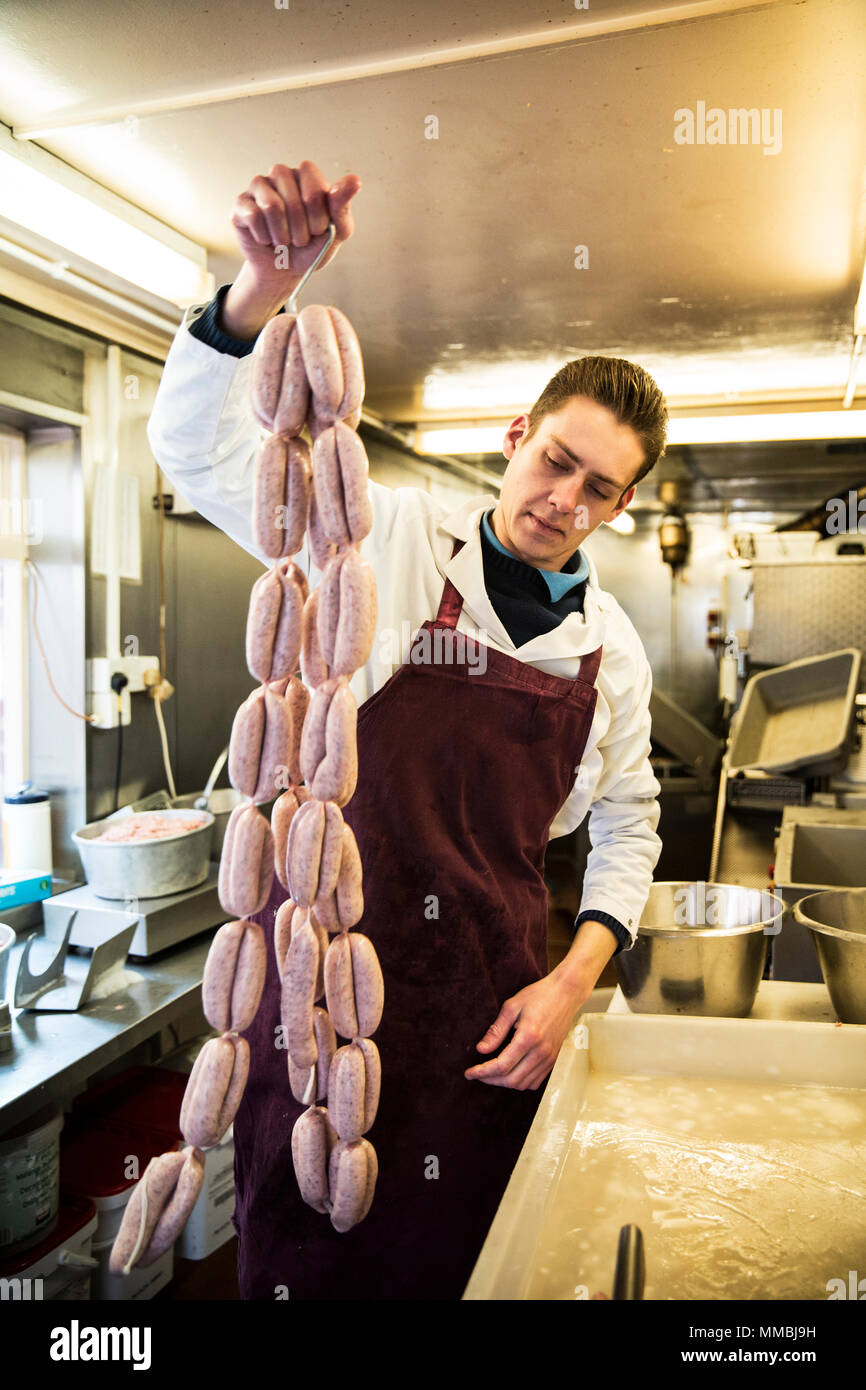 Uomo che indossa il grembiule in piedi in macelleria, azienda grande numero  di freschi salsicce appesi da ganci Foto stock - Alamy