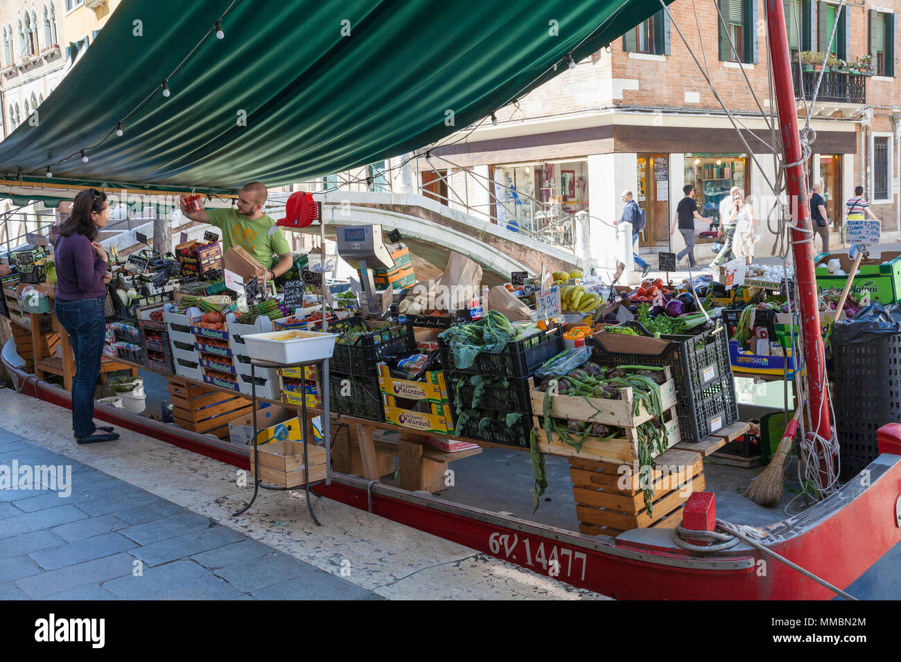 L'uomo la vendita di prodotti freschi, frutta e verdura, da una barca sul Rio di San Barnaba, Campo San Barnaba, Dorsoduro, Venezia, Italia ad un locale woma veneziano Foto Stock