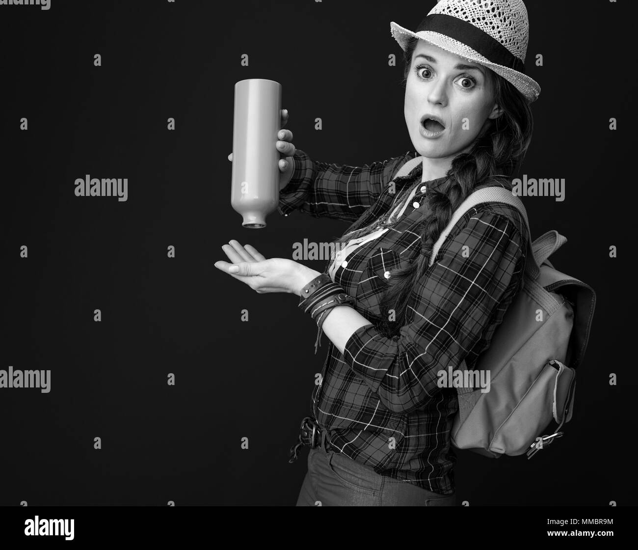La ricerca di luoghi ispiratrice. sorpreso giovane turista donna in un plaid shirt aver lasciato senza acqua in bottiglia isolato su sfondo Foto Stock