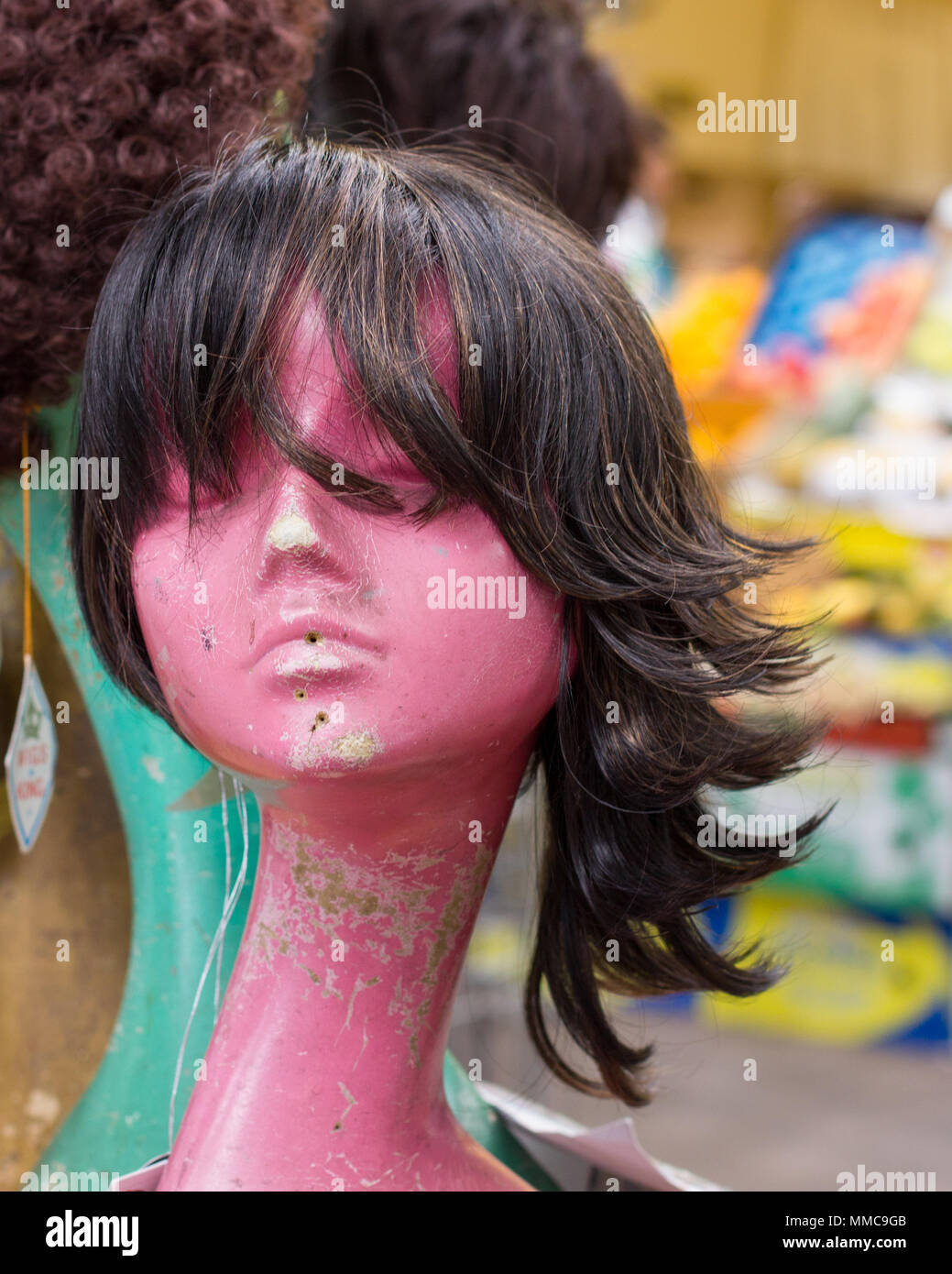 La parrucca appollaiato su un manichino femminile in testa la store window display di Brixton mercato coperto ladies' di moda capelli business di alimentazione, Londra, Regno Unito. Foto Stock