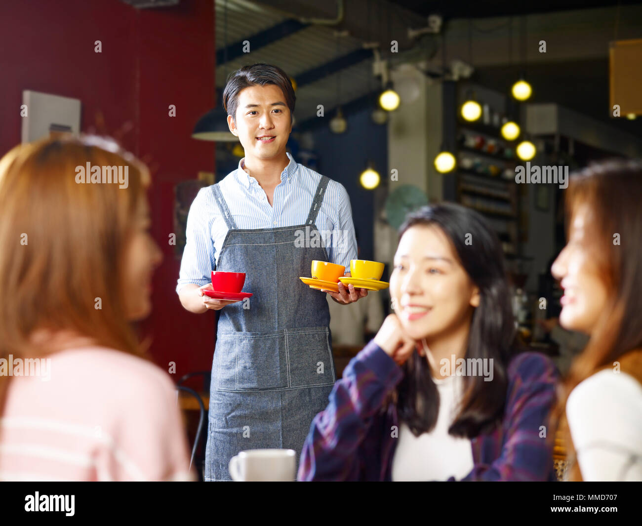 Giovani asiatici cameriere che serve i clienti di sesso femminile nel coffee shop, shot attraverso il vetro di una finestra. Foto Stock
