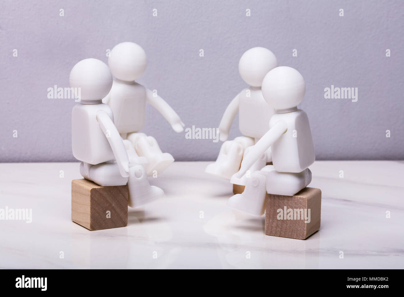 Quattro bianchi statuine umane seduto sul blocco di legno avente riuniti insieme Foto Stock