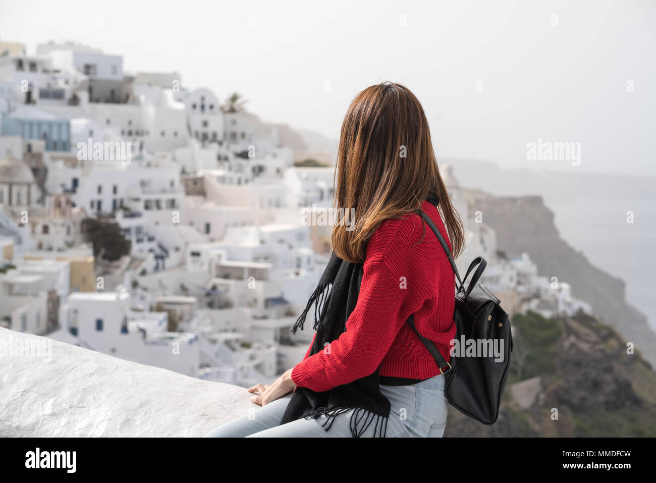 Giovane ragazza asiatica in maglione rosso e nero zaino godetevi il panorama mentre è in vacanza a Santorini, Grecia. Foto Stock