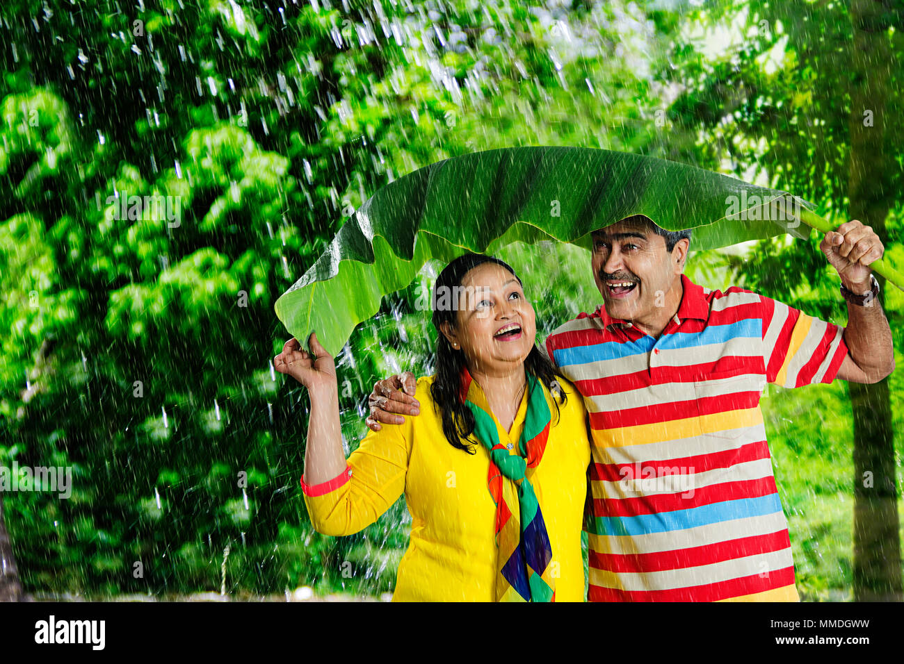 Felice vecchia coppia sotto banana-foglie, proteggere la pioggia avente Fun-Cheerful in giardino Foto Stock