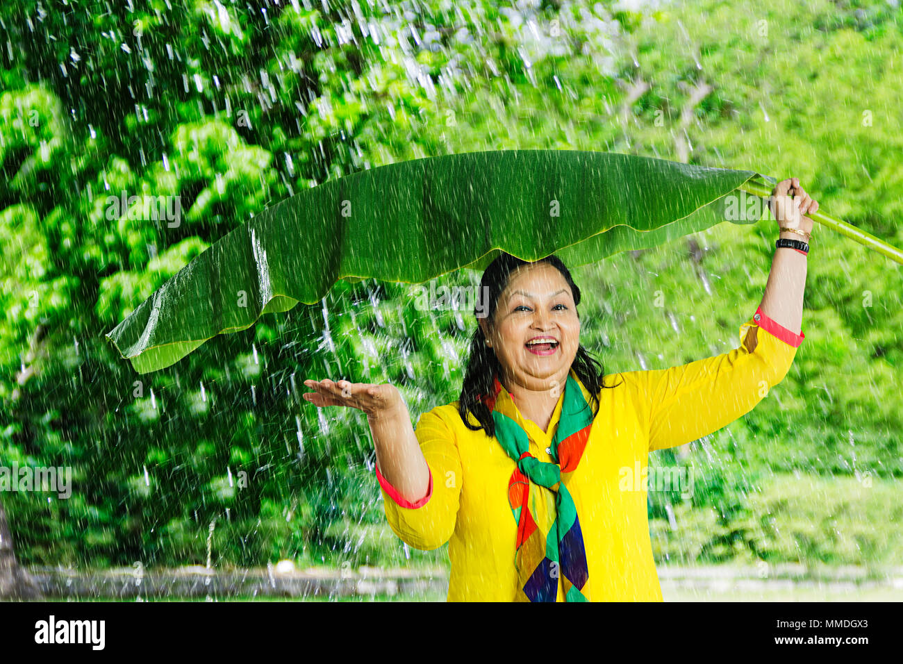 Old Lady sotto Banana-Leaf mise la mano, controllo pioggia godono di giardino Foto Stock