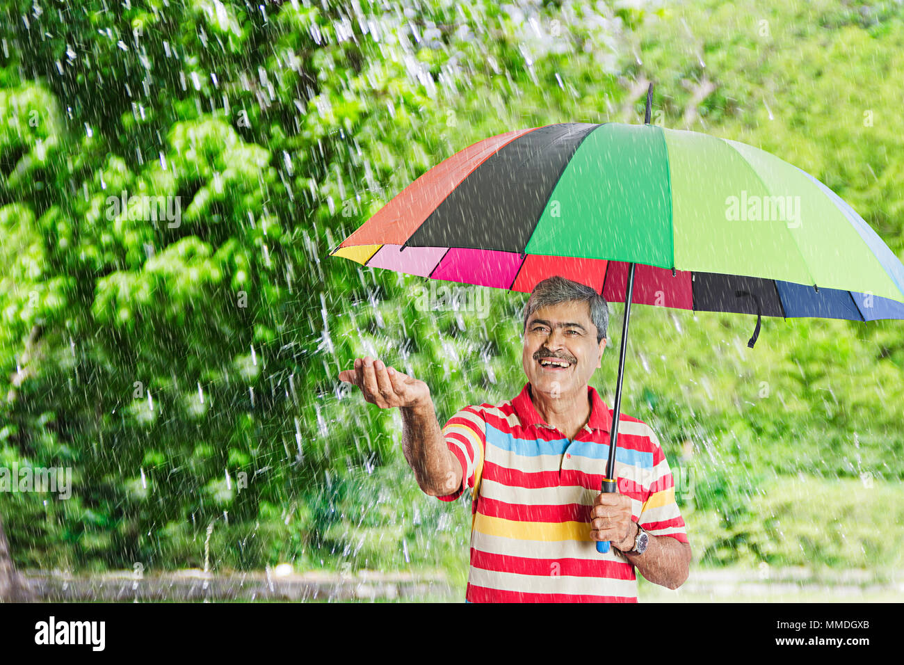 Felice Senior uomo sotto l'ombrello putting-out invece sentire le gocce di pioggia palm Park Foto Stock