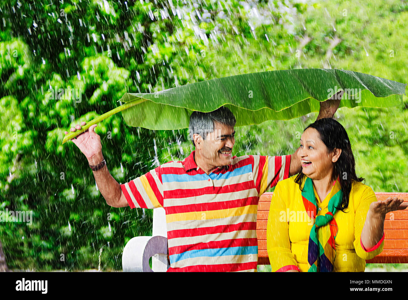 Felice coppia Senior sitting Banco sotto la pioggia Banana-Leaves.Giardino di sicurezza Foto Stock