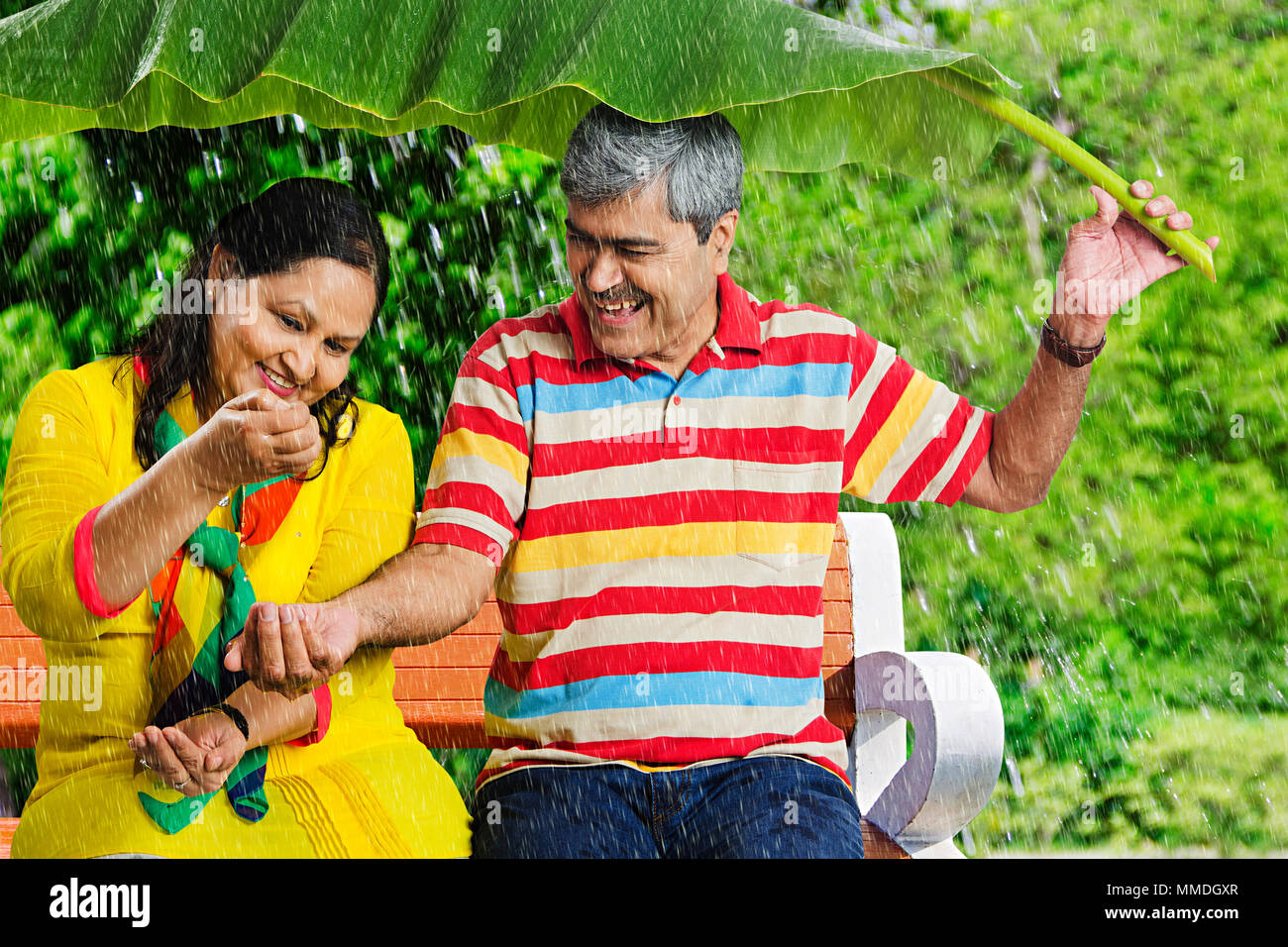 Felice Vecchio Married-Couple Banana-Leaf sotto la pioggia battente. mani divertimento Giardino Foto Stock