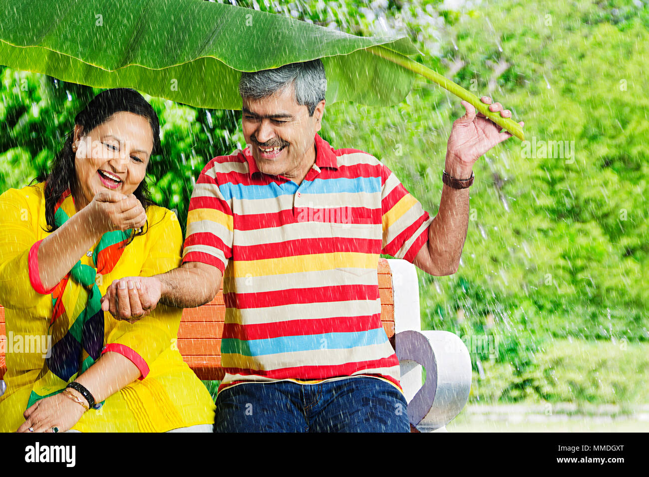 Felice coppia Senior Banana-Leaf sotto la pioggia battente. mani divertimento Giardino Foto Stock