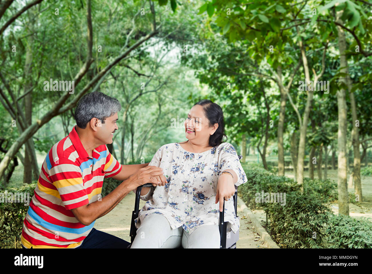 Coppia di anziani in-park, moglie seduta su una sedia a rotelle e marito di parlare Foto Stock