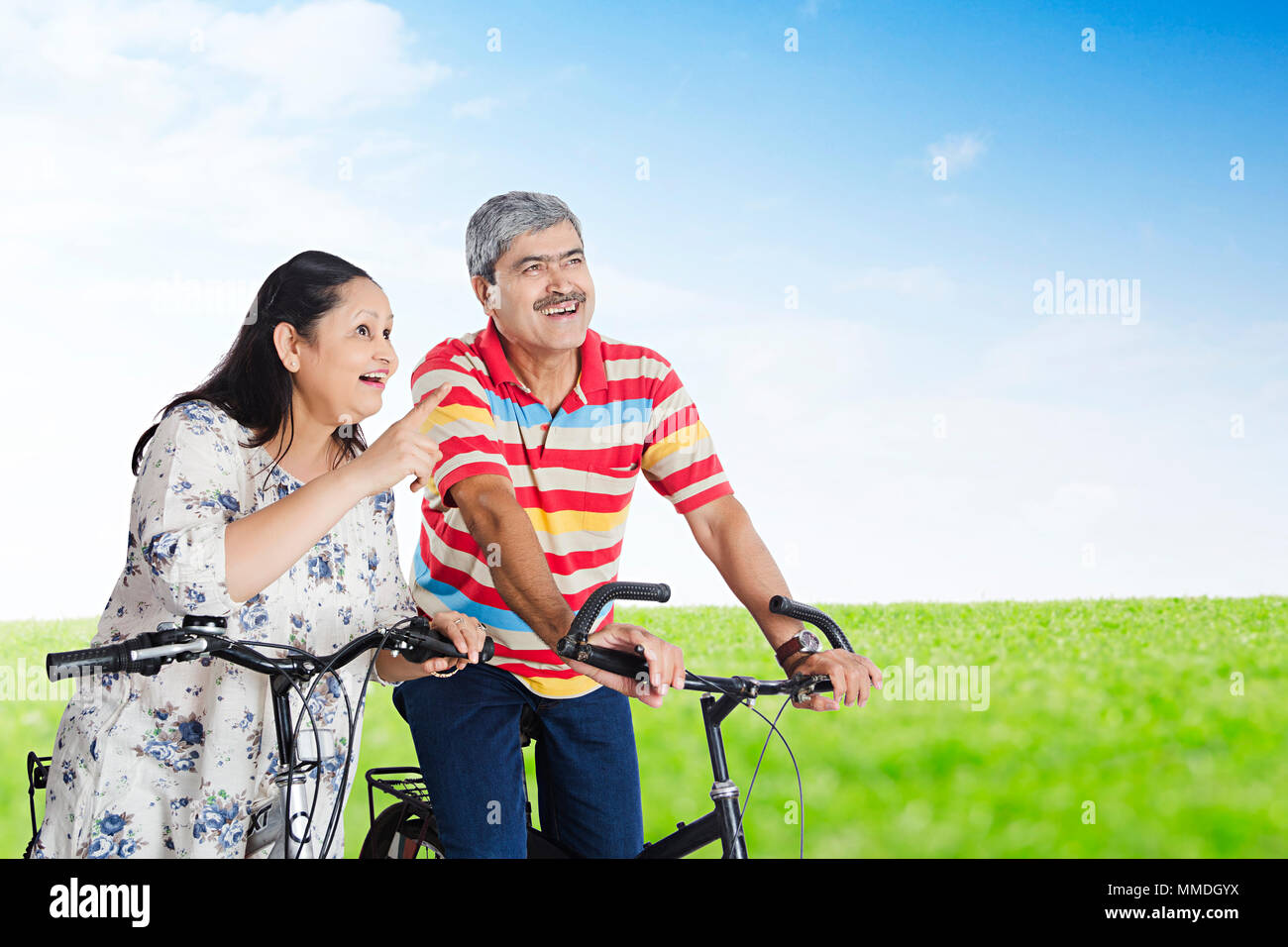 Senior Married-Couple Ciclo di seduta e la moglie puntando verso qualcosa di In-Park Foto Stock
