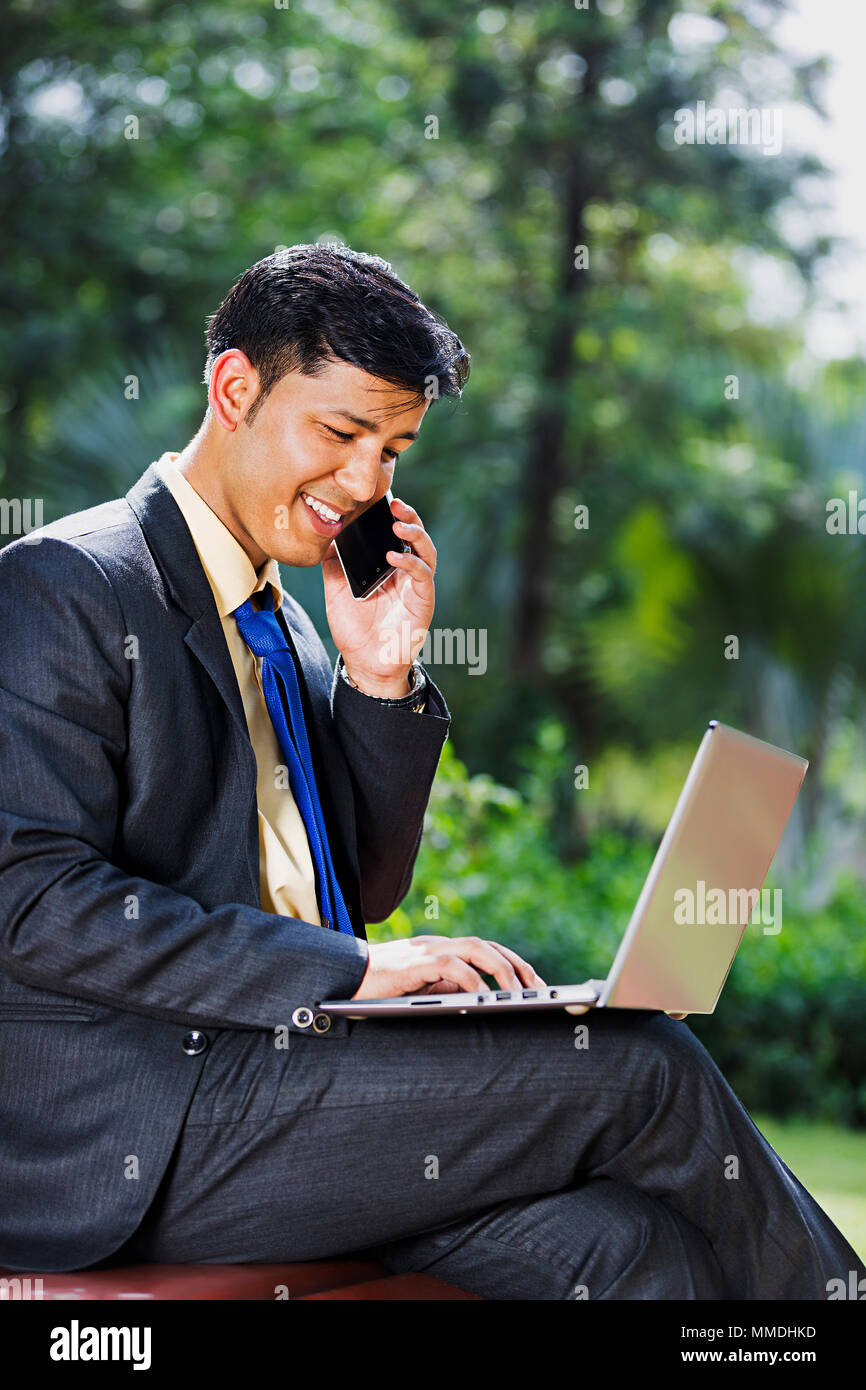 Un maschio di Business Banco seduta utilizzando laptop e parlando Mobile-Phone park Foto Stock