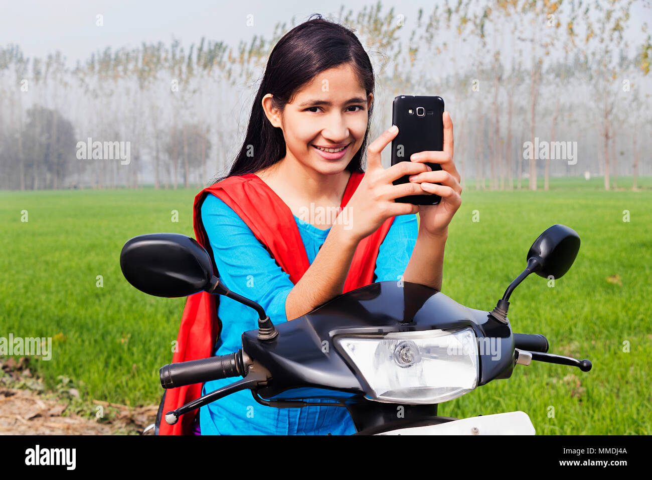 Giovane ragazza seduta Scooty inviare Text-Message Mobile-Phone campo villaggio rurale Foto Stock