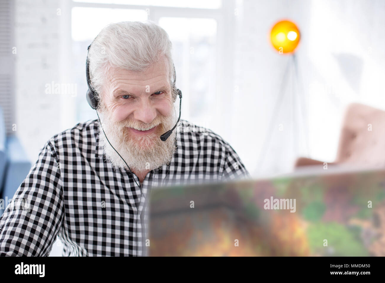 Senior gioioso uomo sorridente durante la riproduzione di un gioco online Foto Stock
