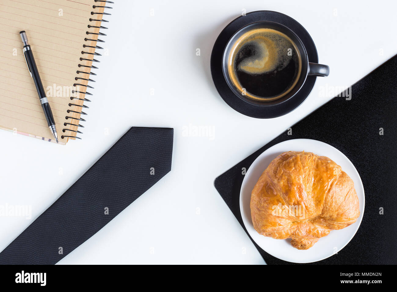 Lay piatto del giorno di mattina per la concezione di business , un caffè e un croissant e cravatta e notebook con penna Foto Stock