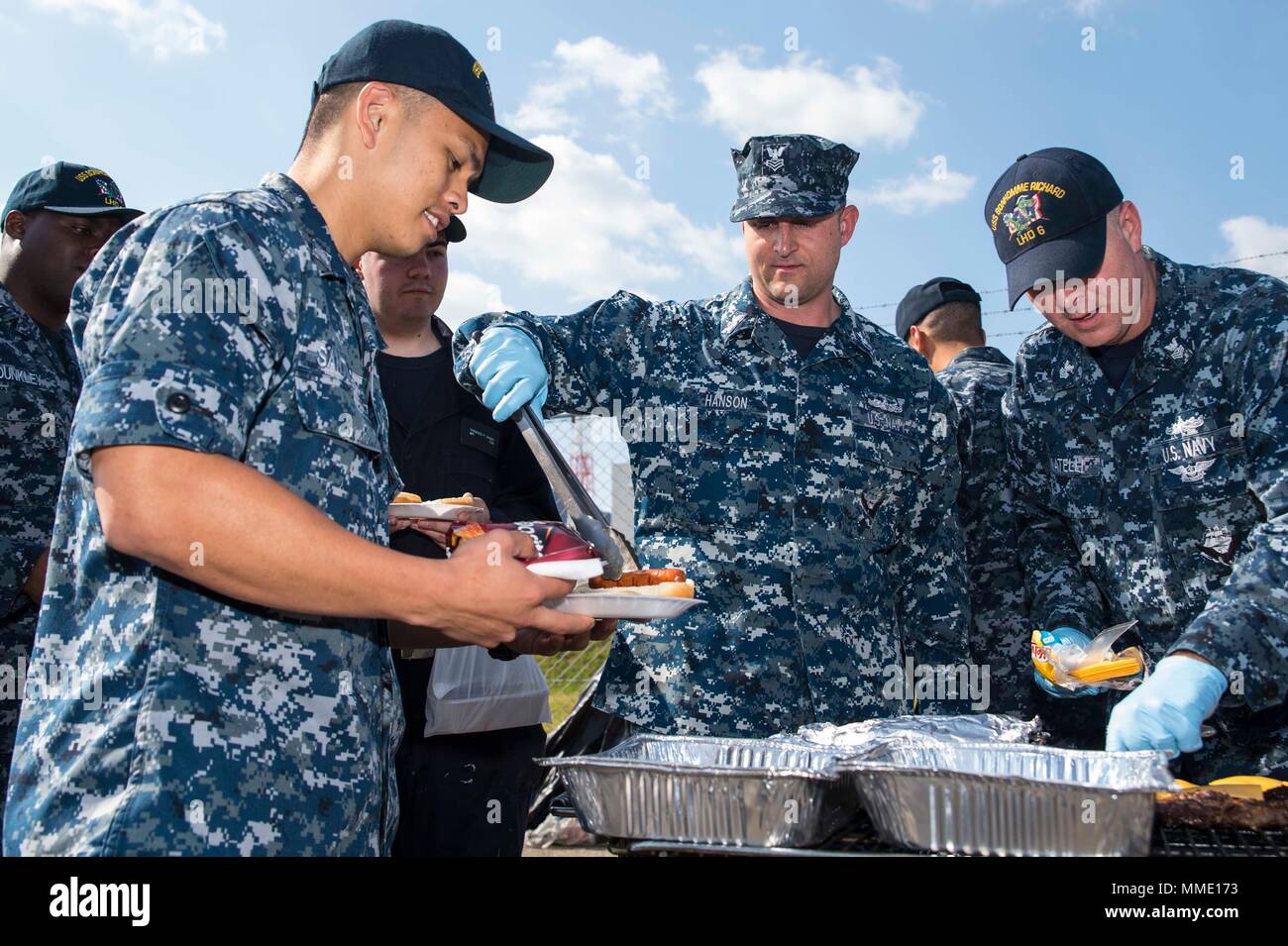 171025-N-XT039-009 SASEBO (ott. 25, 2017) Operazioni Specialist 1a classe Jeffrey Hanson, centro, dal meridiano, Idaho, serve uno specialista operazioni 1a classe Brett Santiago, da San Diego, durante una prima classe Petty Officer Association (FCPOA) "Burger Burn" davanti all'assalto anfibio nave USS Bonhomme Richard (LHD 6). Il FCPOA "Burger Burn" è destinato a raccogliere fondi per un imminente Bonhomme Richard bambini partito per le vacanze. Bonhomme Richard, distribuita a Sasebo, Giappone, serve in avanti per fornire una rapida capacità di risposta in caso di emergenza regionale o naturale Foto Stock