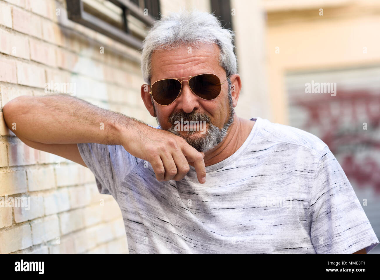 Coppia uomo sorridente in telecamera in background urbano. Senior maschio  con i capelli bianchi e la barba di indossare un abbigliamento informale e  aviator occhiali da sole Foto stock - Alamy