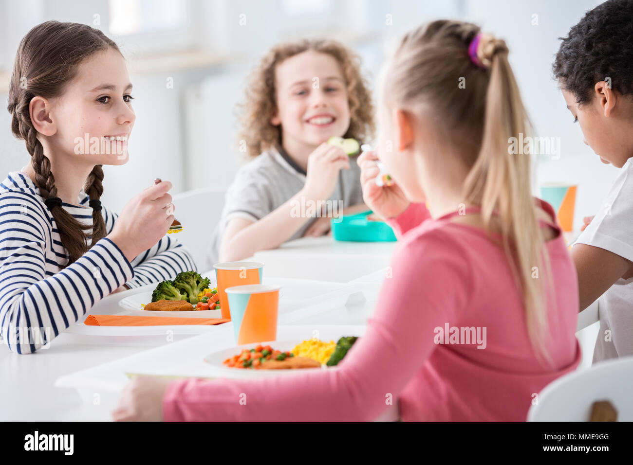 Ragazza sorridente di mangiare le verdure durante la pausa pranzo con gli amici a scuola Foto Stock