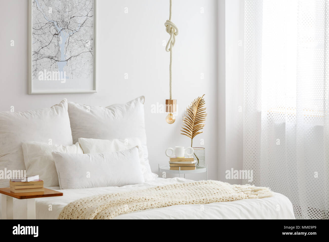 Una semplice lampada lampada su una corda appesa sopra il letto con  lenzuola bianche, libri e