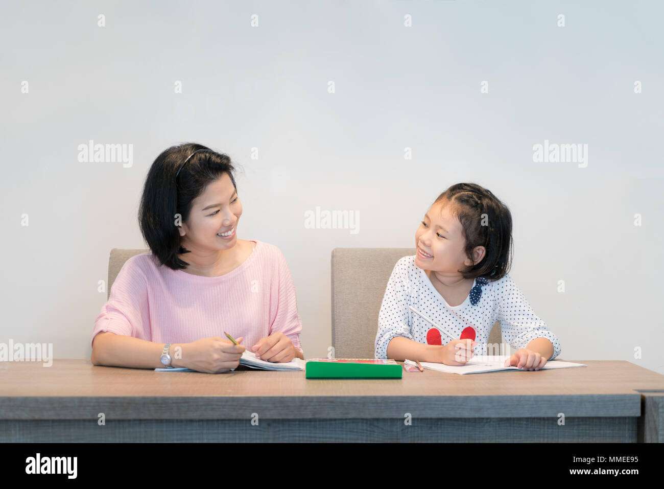 Felice famiglia asiatica. Asian madre e figlia insieme il disegno e la vernice nel libro. Donna adulta aiuta il bambino ragazza per fare i compiti a casa. Foto Stock