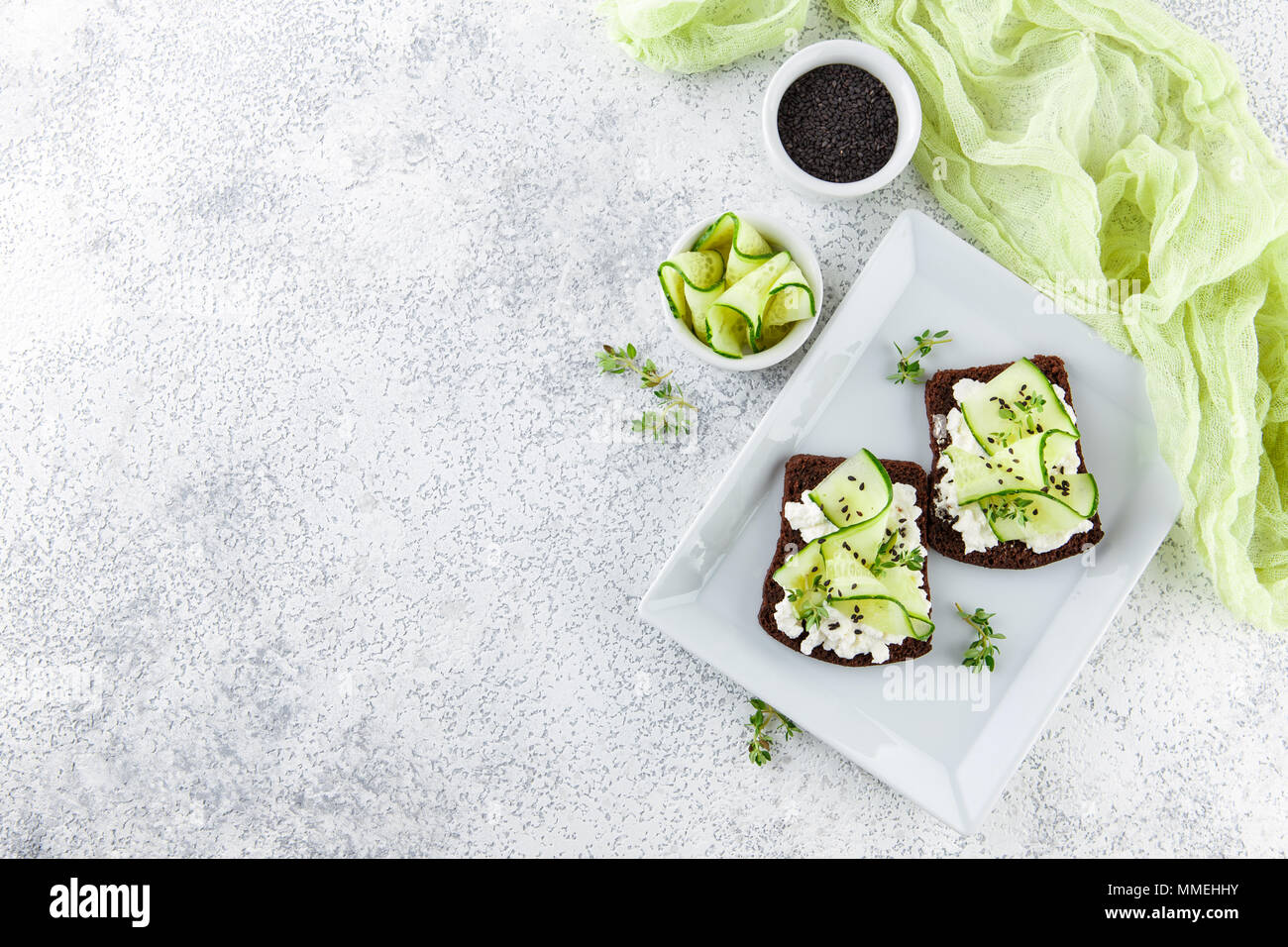 Crostini di pane di segale con ricotta, cetriolo e sesamo nero su grigio ardesia e pietra o calcestruzzo sfondo. Foto Stock