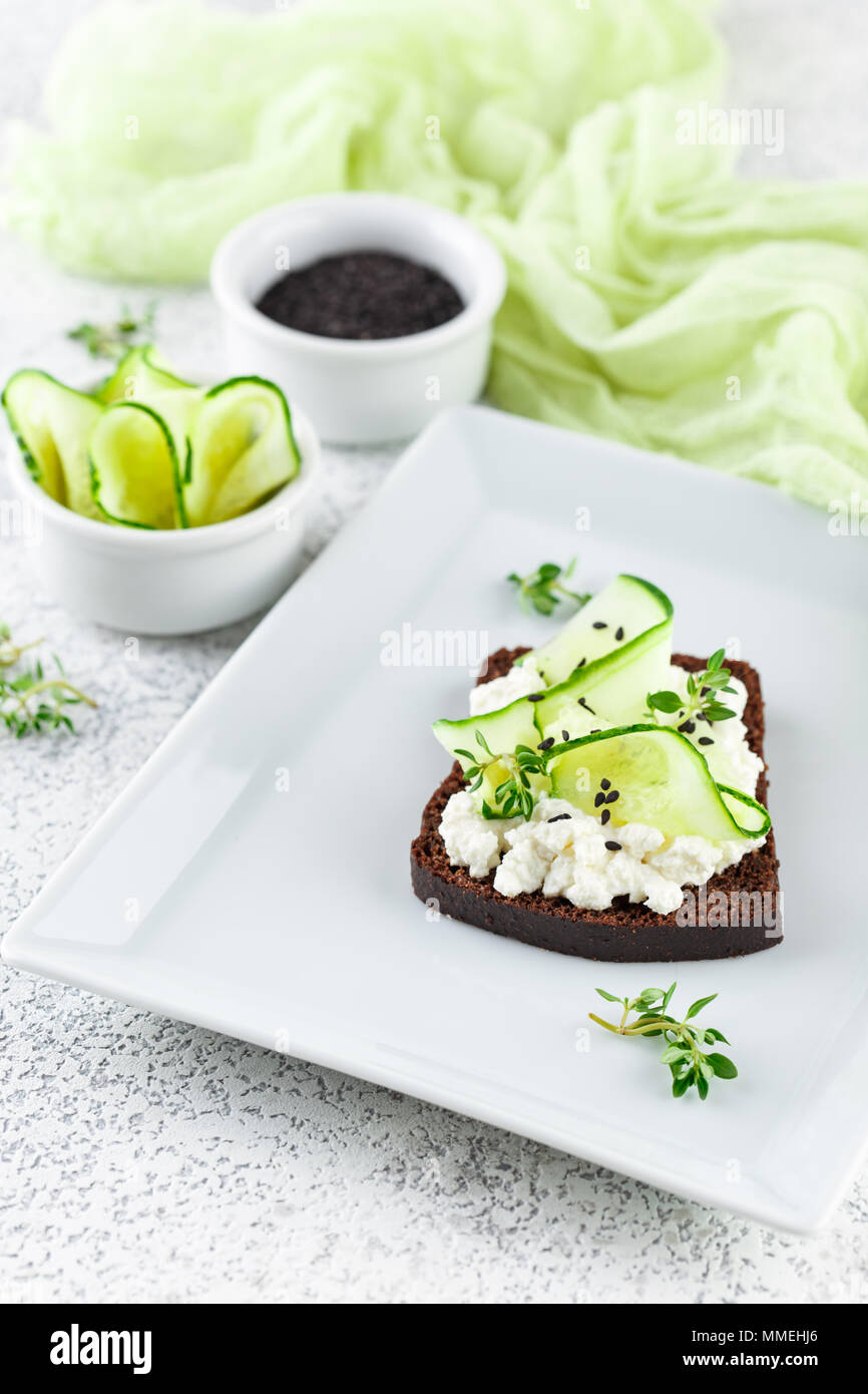 Crostini di pane di segale con ricotta, cetriolo e sesamo nero su grigio ardesia e pietra o calcestruzzo sfondo. Foto Stock