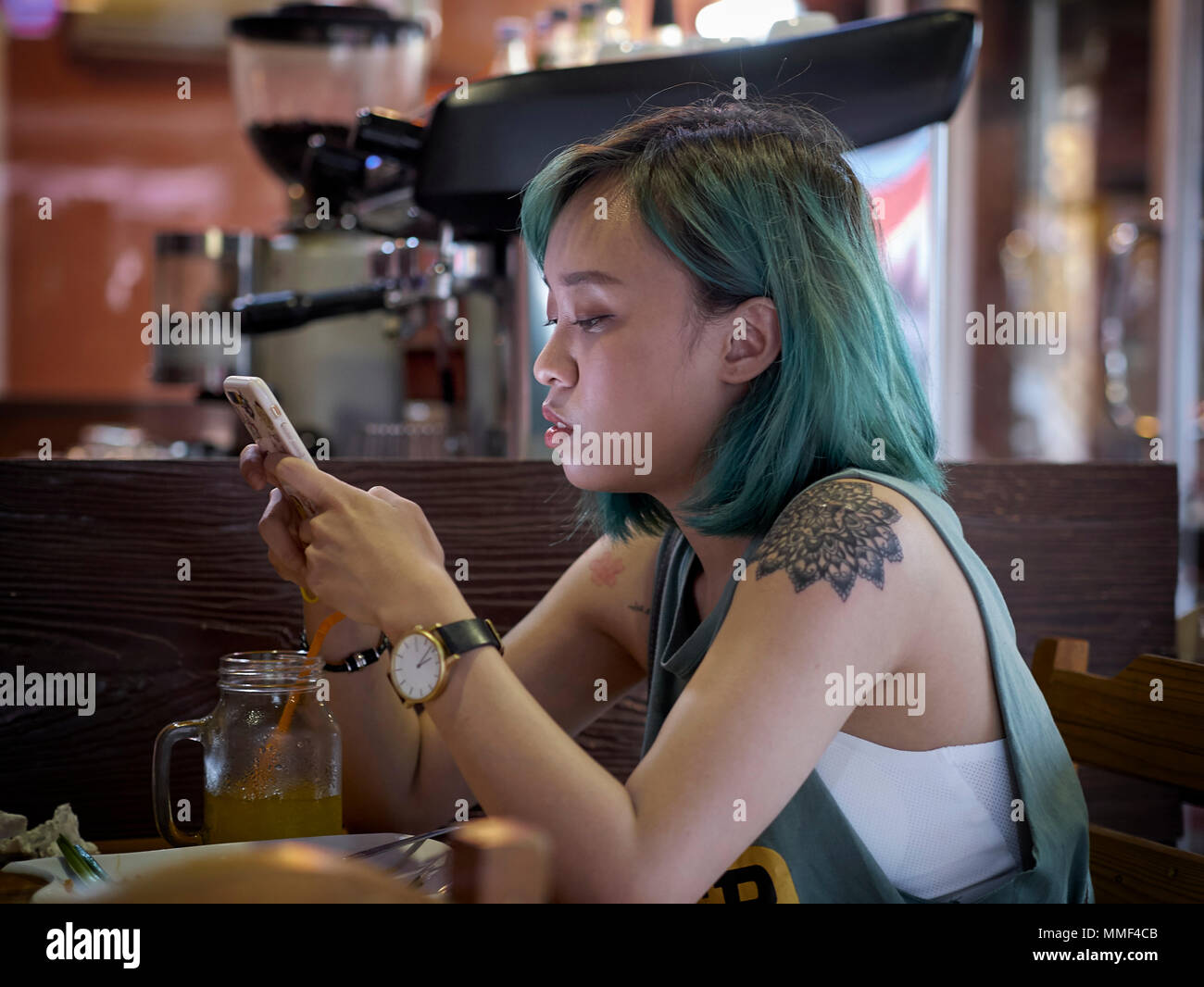 Donna con lo smartphone, vicino. Femmina con i capelli verdi e la spalla tattoo. Foto Stock