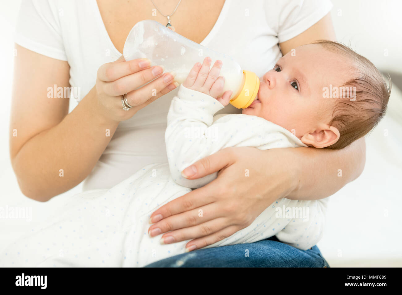 Primo piano della giovane donna mentre tiene il suo bambino sul giro e dandogli una bottiglia di latte Foto Stock