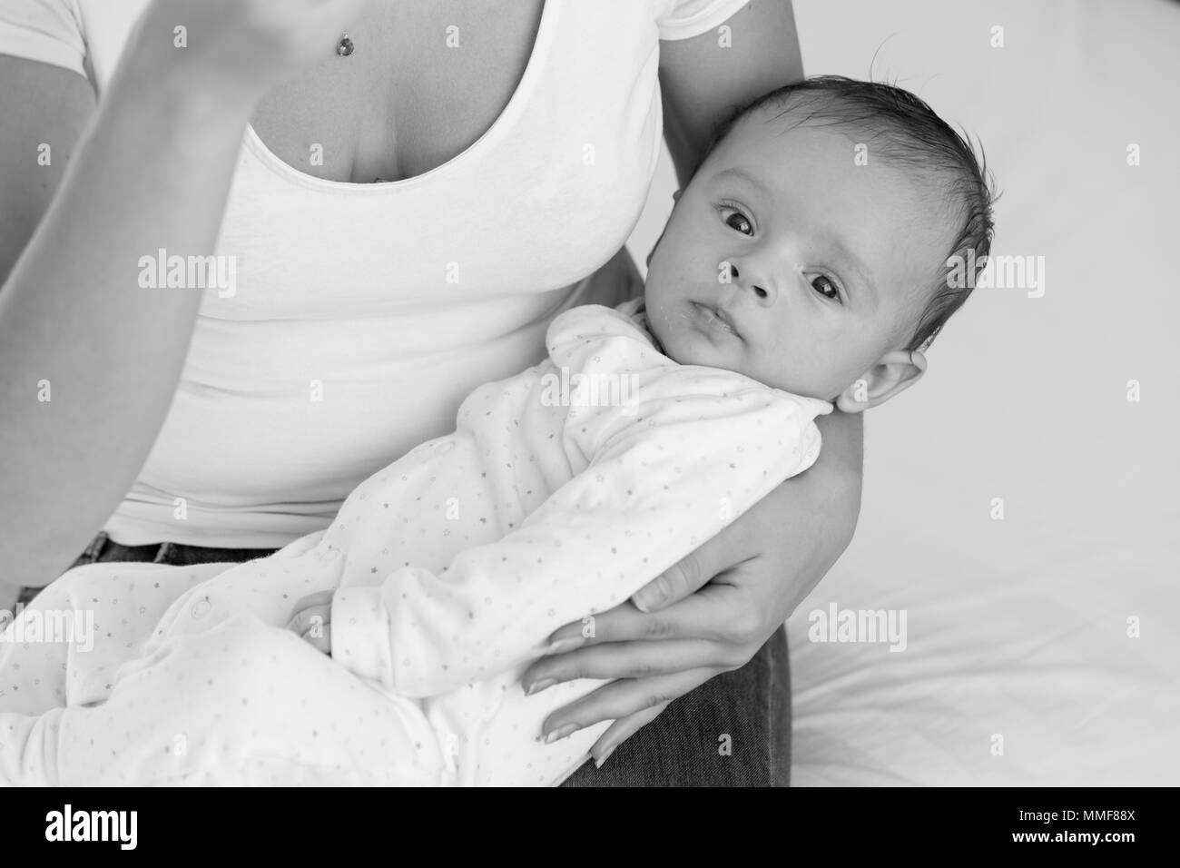 Ritratto in bianco e nero del simpatico bimbo giacente sul giro delle madri e cercando nella fotocamera Foto Stock