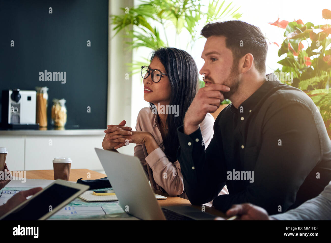 Diversi colleghi parlano seduti insieme ad un tavolo per riunioni in un ufficio avente una riunione Foto Stock